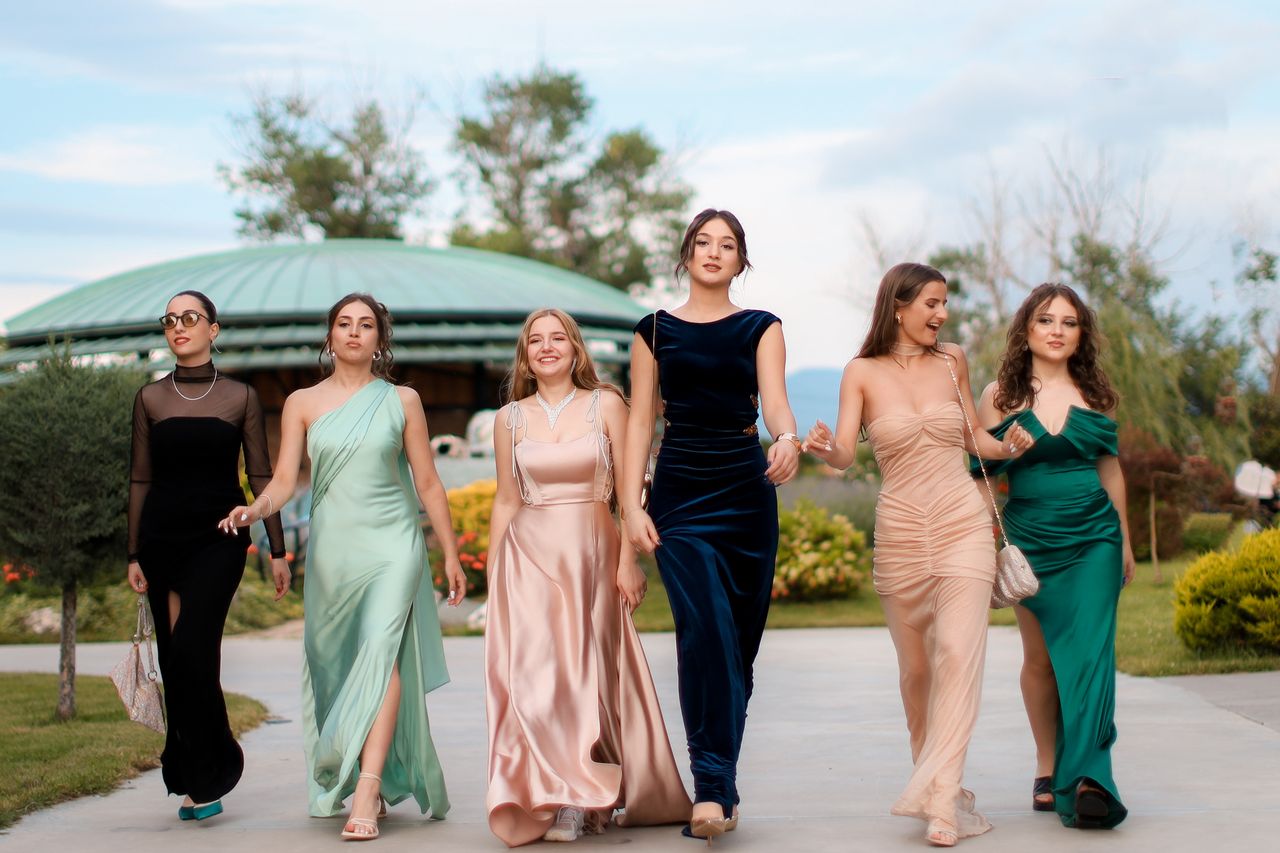 A group of six women in elegant evening dresses walking confidently outdoors, showcasing fashion and style.